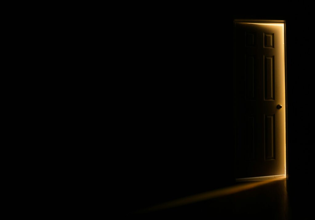 Partially open door with warm light shining into a dark room, symbolizing distance and what can’t be seen