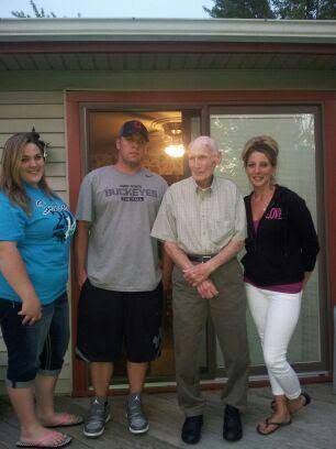 A grandfather standing with his three grandchildren during a family gathering.
