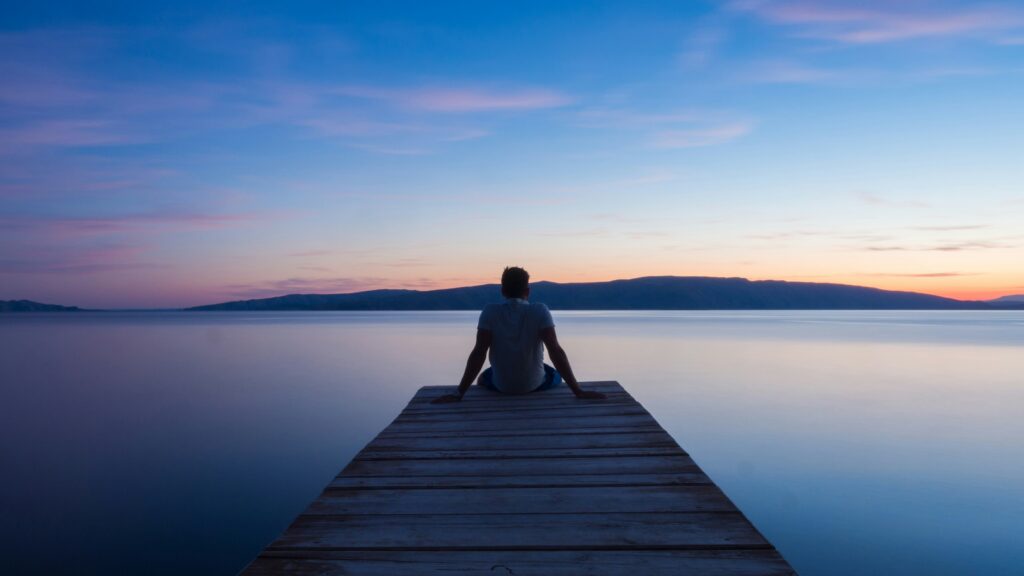 Person sitting on a dock at sunset reflecting on life and past mistakes