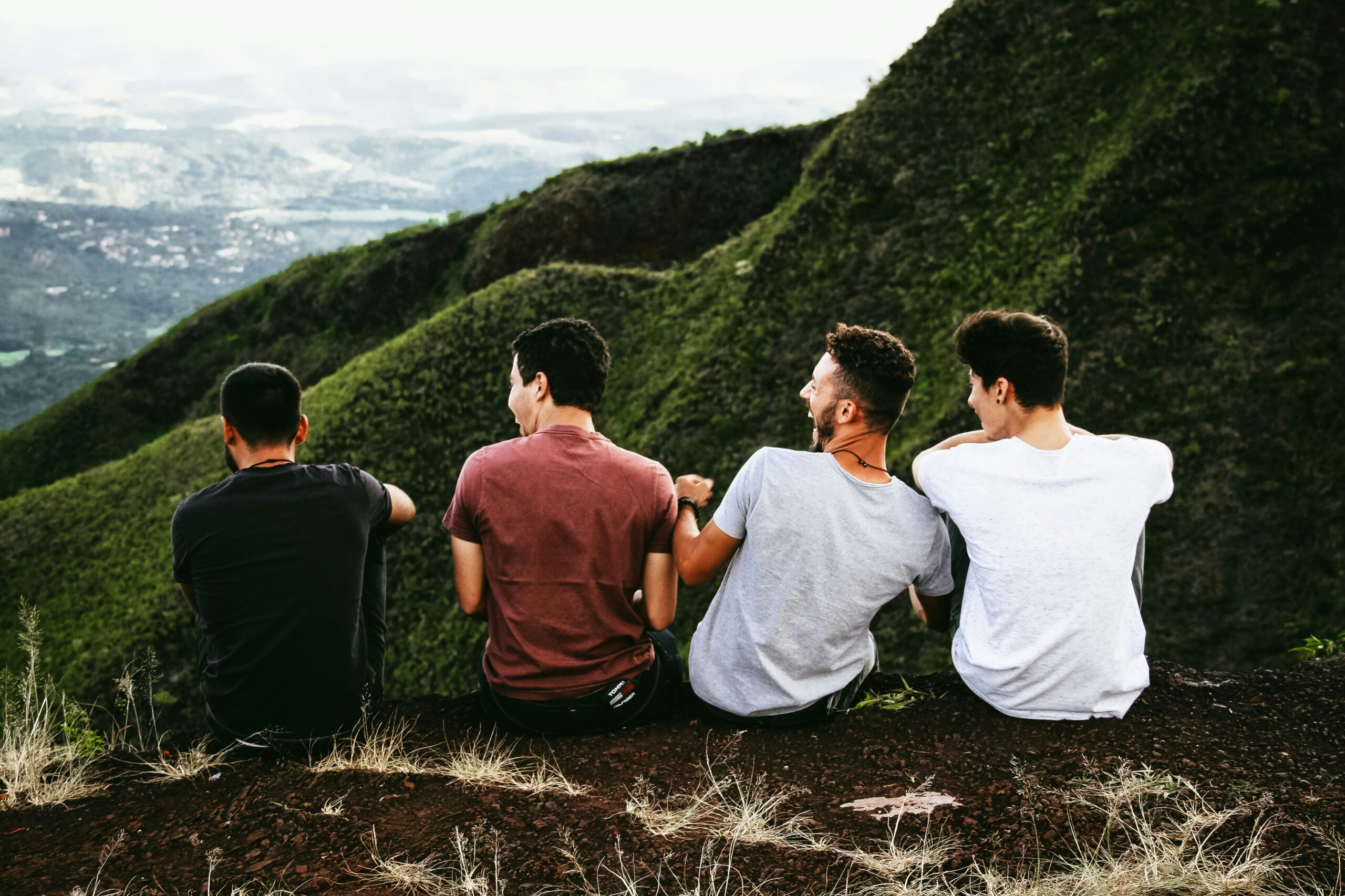 Four friends sitting on a hillside overlooking a valley and mountains