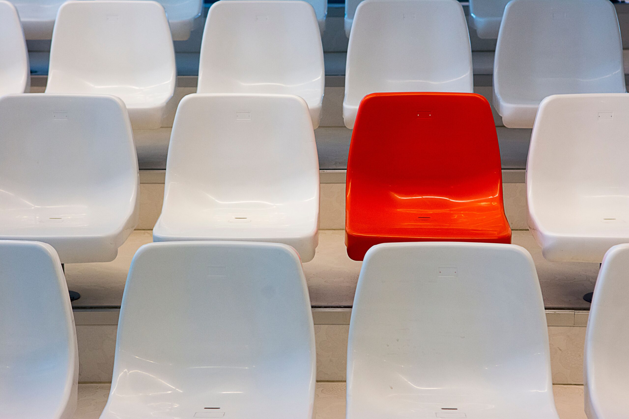 Single red chair surrounded by rows of white chairs, symbolizing identity and belonging