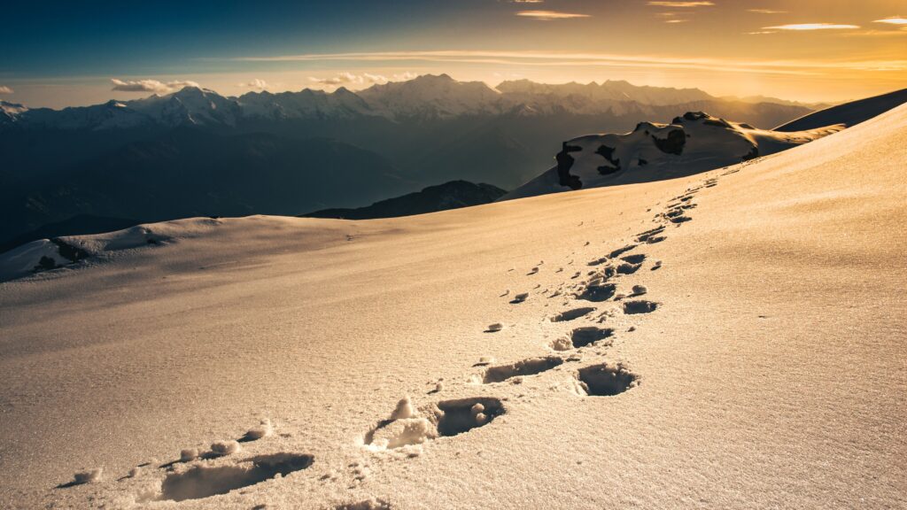Footprints leading across a snowy mountain ridge toward distant peaks