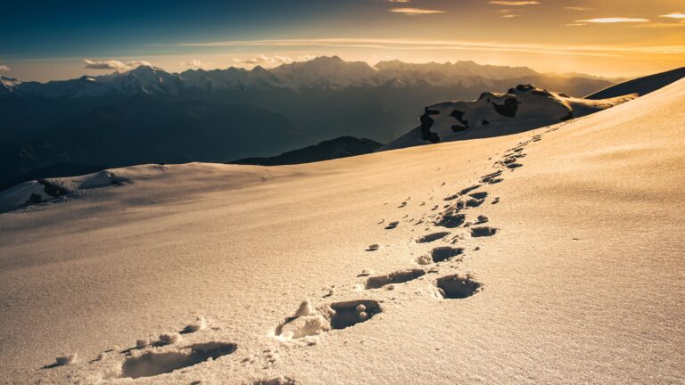 Footprints leading across a snowy mountain ridge toward distant peaks