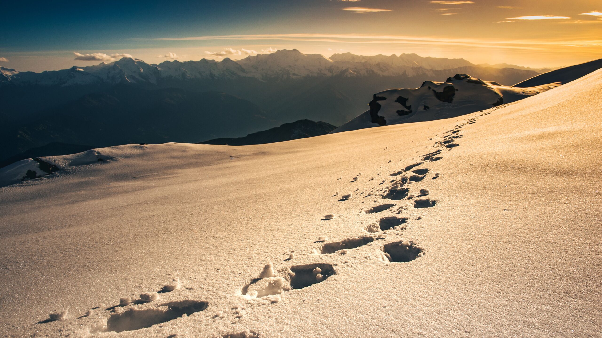 Footprints leading across a snowy mountain ridge toward distant peaks